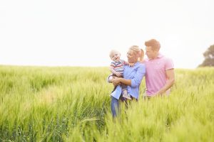 Family Walking In Field Carrying Young Baby Son